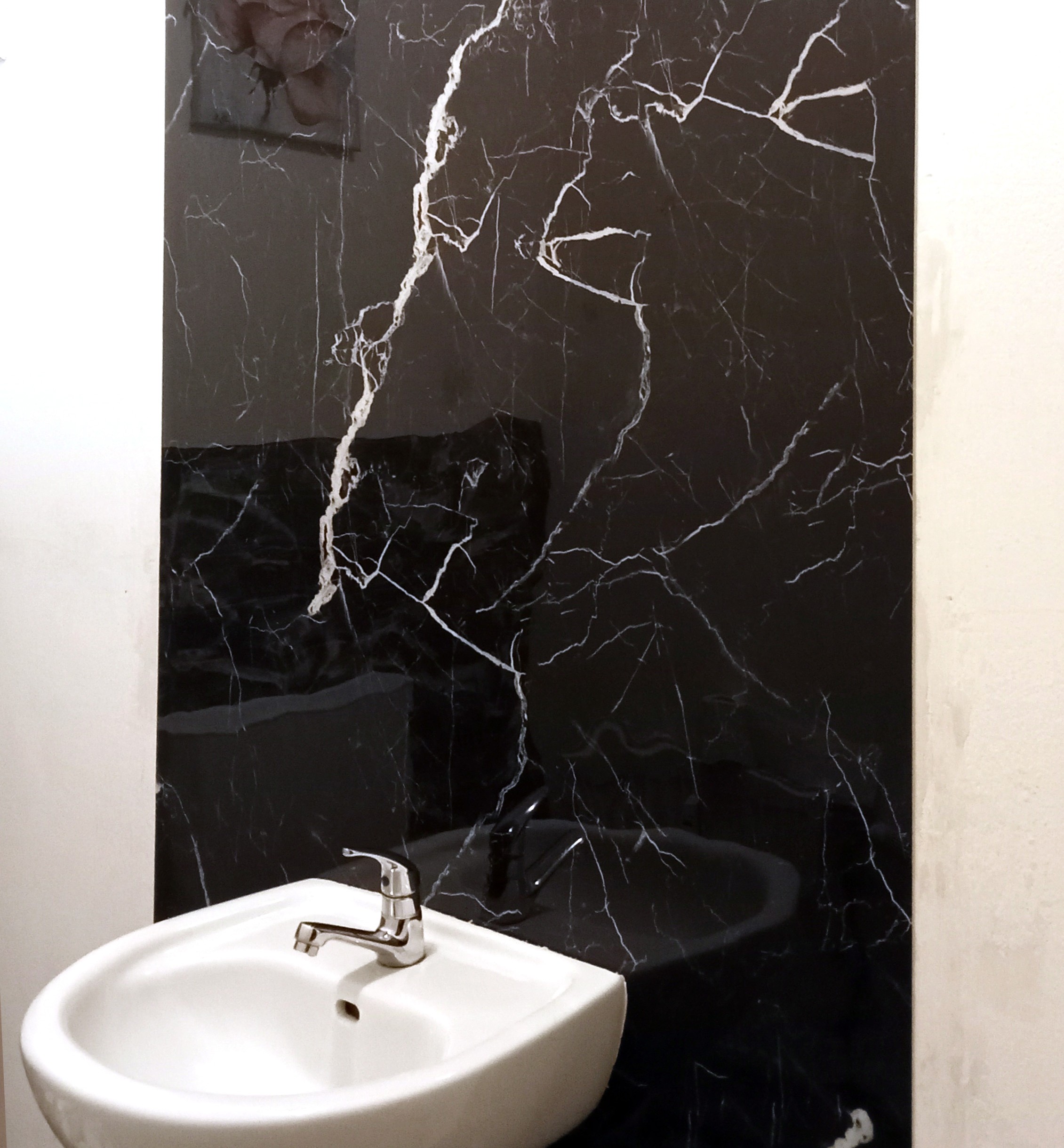 Eine Klebefolie mit schwarzer Marmor-Optik als Statement Piece in einem weißen Badezimmer.