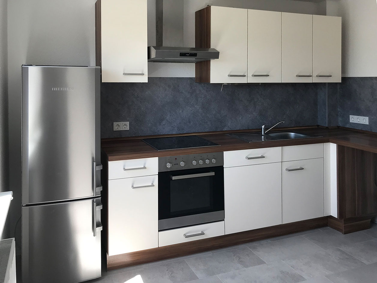 Moderne Küche mit Kühlschrank, weißen Schränken, Herd und Spüle, dunkler Rückwand und Holzarbeitsplatte.